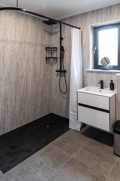 A modern and stylish bathroom featuring a walk in shower. Natural light comes in through the window above the sink which is to the right of the shower.