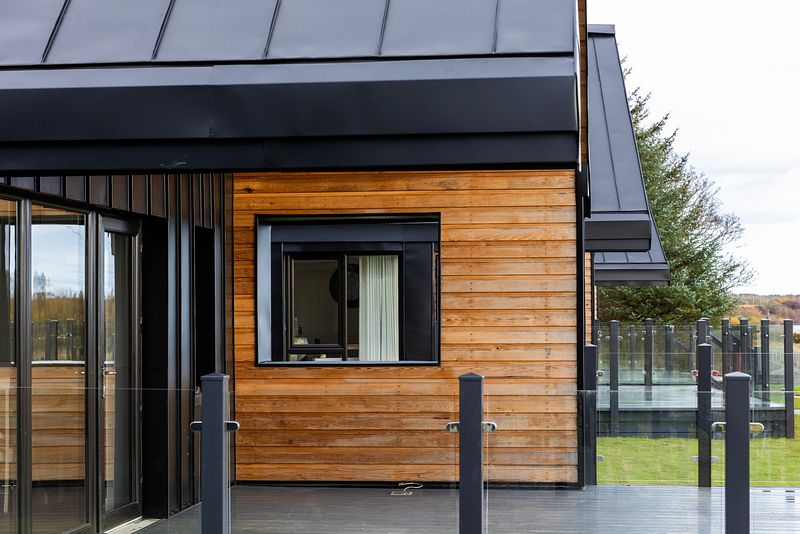 The stylish and modern entrance to a chalet can be seen from a side view. More chalets can be seen in the background.