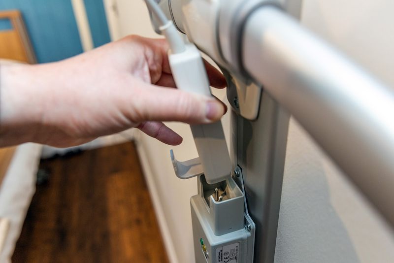 A hand is holding the grey control handset for the bed and is placing it into the grey charging dock.