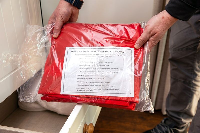 A red evacuation slide sheet inside a plastic package is being held up to the camera. The instructions can be seen on inside the packaging also.