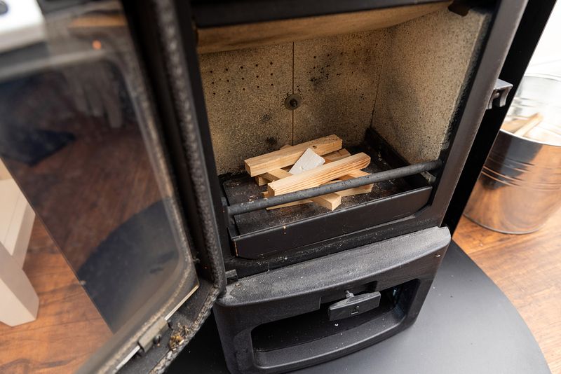 The stove is open and small pieces of wood are arranged within.